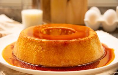 Fotografia mostra uma torta com textura delicada e cremosa, coberta por uma calda de caramelo dourada e servida em um prato branco. Fotografia mostra uma torta com textura delicada e cremosa, coberta por uma calda de caramelo dourada e servida em um prato branco.