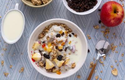 Fotografia em tons de branco com um pote branco ao centro. Dentro do pote existe uma receita de cereal com frutas secas e banana.