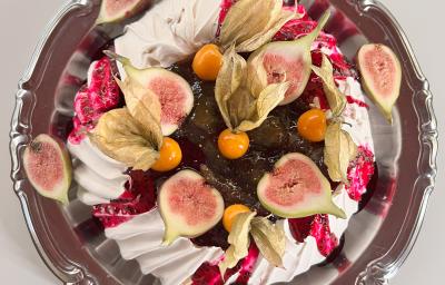 Fotografia em tons de rosa com uma sobremesa decorada com figo e pitaya ao centro. A sobremesa é um pavlova tropical feito com geleia de pitaya Fotografia em tons de rosa com uma sobremesa decorada com figo e pitaya ao centro. A sobremesa é um pavlova tropical feito com geleia de pitaya