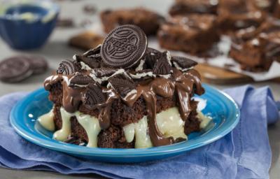 fotografia em tons de azul e marrom, contém um pano azul com um prato redondo e azul, um bolo com creme de avelã e biscoitos de chocolate por cima para decorar