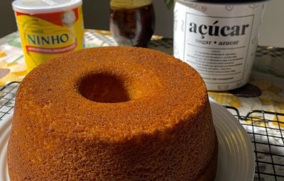 Fotografia de um bolo de ninho inteiro, assado na forma com furo no centro, sobre um prato branco e raso.