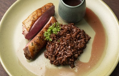 foto da Receita de Pato Selado com Risoto de Vinho Tinto, Alho Negro e Chocolate servido em um prato redondo e vista de cima