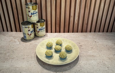 Fotografia em tons de verde em uma bancada em tons de bege, Leite Moça ao fundo e um prato com brigadeiros ao centro.