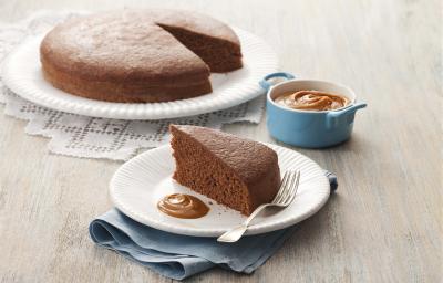 fotografia em tons de cinza e marrom de uma bancada cinza vista de frente. Contém um prato redondo branco, com um bolo de chocolate sem uma fatia. Ao lado outro prato com a fatia de bolo e um garfo ao lado para servir.
