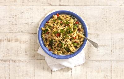 em uma mesa de madeira na cor cinza, contém um recipiente na cor azul que comporta a salada de macarrão. em uma mesa de madeira na cor cinza, contém um recipiente na cor azul que comporta a salada de macarrão.