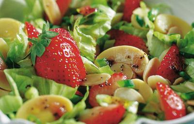 Fotografia em tons de verde em uma bancada de madeira azul com um recipiente redondo e fundo com a salada primavera composta por alface, cogumelo e morango.