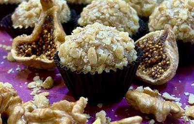 Foto de receita de Brigadeiro de Figo com Nozes. Observa-se o brigadeiro com nozes picadas em volta em uma forminha preta, com figos secos cortados ao lado e nozes na projeção da frente. Ao fundo, mais brigadeiros. Foto de receita de Brigadeiro de Figo com Nozes. Observa-se o brigadeiro com nozes picadas em volta em uma forminha preta, com figos secos cortados ao lado e nozes na projeção da frente. Ao fundo, mais brigadeiros.