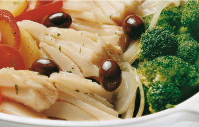 Fotografia em tons de verde e vermelho em uma bancada de madeira em uma mesa com uma toalha cinza, um refratário oval branco com bacalhau com tomate, batata e brócolis. Fotografia em tons de verde e vermelho em uma bancada de madeira em uma mesa com uma toalha cinza, um refratário oval branco com bacalhau com tomate, batata e brócolis.