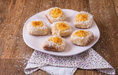 Foto da receita de pão com creme de leite moça, servidos em um prato rosa claro, com coco ralado salpicado, em uma bancada de madeira decorada com um pano de motivos florais Foto da receita de pão com creme de leite moça, servidos em um prato rosa claro, com coco ralado salpicado, em uma bancada de madeira decorada com um pano de motivos florais