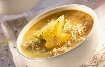Fotografia de um flan de carambola com coco ralado por cima, limão e uma rodela de carambola. O creme está dentro de um recipiente pequeno de vidro na cor branco, que está sobre uma toalha de mesa branca com detalhes dourados. Fotografia de um flan de carambola com coco ralado por cima, limão e uma rodela de carambola. O creme está dentro de um recipiente pequeno de vidro na cor branco, que está sobre uma toalha de mesa branca com detalhes dourados.