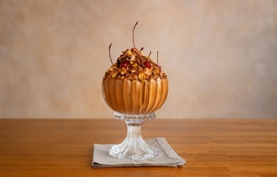 Fotografia em tons claros da Mousse Floresta Negra cremosa e aerada, servida em taça de vidro, decorada com cerejas, avelãs tostadas e raspas de chocolate. Uma sobremesa elegante, perfeita para impressionar em ocasiões especiais!