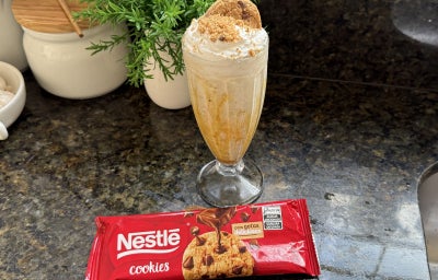 Foto da receita de Milkshake de Cookies e Caramelo, servido em um copo alto, numa bancada de mármore com um pacote de Cookies Nestlé Tradicional à frente