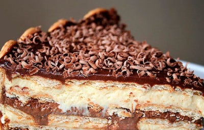 Fatia de pavê com camadas de creme, chocolate e biscoito, coberta com raspas de chocolate.