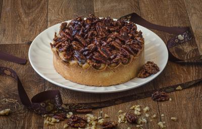 Foto da receita de Torta de Caramelo Salgado e Castanhas Caramelizadas, servida num prato redondo branco, sobre uma bancada de madeira, decorada com uma fita de páscoa e castanhas picadas Foto da receita de Torta de Caramelo Salgado e Castanhas Caramelizadas, servida num prato redondo branco, sobre uma bancada de madeira, decorada com uma fita de páscoa e castanhas picadas