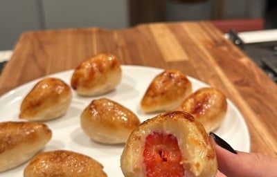 Fotografia de mini coxinhas de morango com massa dourada e brilho leve, recheadas com morango inteiro no centro. Uma releitura criativa e irresistível do clássico salgado, agora em versão doce, perfeita para surpreender em festas e sobremesas!