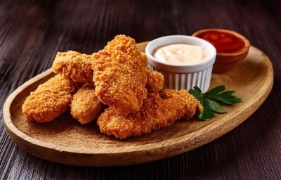 Fotografia mostra tiras de frango empanado e molhos ao lado. Fotografia mostra tiras de frango empanado e molhos ao lado.