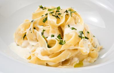 fotografia em tons de branco e amarelo tirada de um prato redondo branco, que contém um macarrão com requeijão e manjericão por cima.