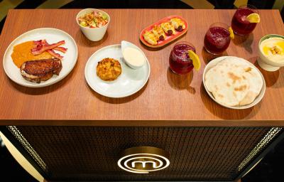 Fotografia de uma mesa de madeira com um brunch com pão sírio, hommus, ovos, frutas, massa folhada, creme inglês de requeijão, crumble de banana e torrada. Todas as partes estão porcionadas em recipientes brancos e separados. Fotografia de uma mesa de madeira com um brunch com pão sírio, hommus, ovos, frutas, massa folhada, creme inglês de requeijão, crumble de banana e torrada. Todas as partes estão porcionadas em recipientes brancos e separados.