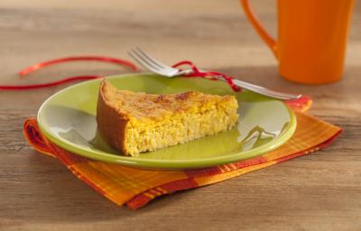 Em uma mesa contém um pano em tons laranja e vermelho, por cima, um prato na cor verde que comporta uma fatia de bolo. Ao lado do prato um garfo de metal e uma xicara laranja. Em uma mesa contém um pano em tons laranja e vermelho, por cima, um prato na cor verde que comporta uma fatia de bolo. Ao lado do prato um garfo de metal e uma xicara laranja.