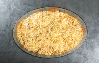 Fotografia em tons de cinza com uma travessa de vidro ao cento. Dentro da travessa existe uma receita de fricassê vegetariano feita com legumes e batata palha.