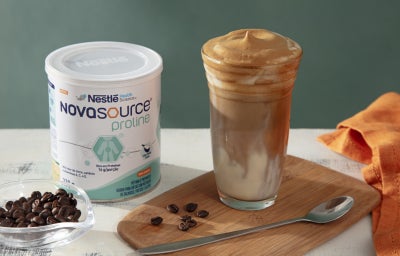 Foto da receita de café gelado cremoso servido em um copo de vidro alto sobre uma tábua de madeira com uma embalagem de novasource proline ao lado Foto da receita de café gelado cremoso servido em um copo de vidro alto sobre uma tábua de madeira com uma embalagem de novasource proline ao lado