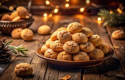 Fotografia em tons marrrom com um prato marrom ao centro. Em cima do prato existe vários biscoitos amaretti polvilhados com açúcar de confeiteiro. Fotografia em tons marrrom com um prato marrom ao centro. Em cima do prato existe vários biscoitos amaretti polvilhados com açúcar de confeiteiro.