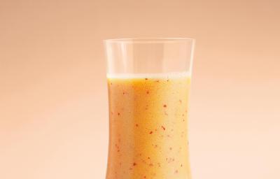 Fotografia em tons de laranja em um fundo laranja e um copo de vidro alto e largo com o suco de acerola, maracujá, pêssego e laranja dentro dele. Fotografia em tons de laranja em um fundo laranja e um copo de vidro alto e largo com o suco de acerola, maracujá, pêssego e laranja dentro dele.