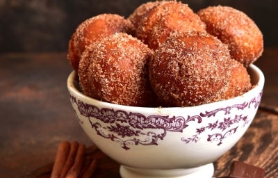 Em cima de uma mesa, tigela com bolinhos redondo, polvilhado com açúcar e canela. Em cima de uma mesa, tigela com bolinhos redondo, polvilhado com açúcar e canela.