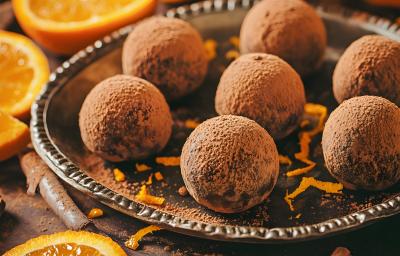 Fotografia mostra Pequenas bolinhas de trufa de chocolate cobertas por uma camada generosa de cacau em pó, ao lado rodelas de laranja. Fotografia mostra Pequenas bolinhas de trufa de chocolate cobertas por uma camada generosa de cacau em pó, ao lado rodelas de laranja.