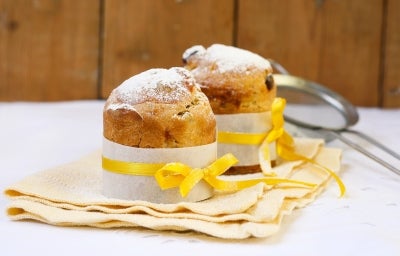 Fotografia mostra um mini panetone em forminha branca, com um laço amarelo em volta.