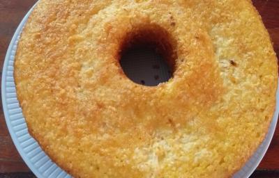 Fotografia em tons de bege em uma bancada de madeira escura, um prato branco redondo e o bolo de milho por cima.. Fotografia em tons de bege em uma bancada de madeira escura, um prato branco redondo e o bolo de milho por cima..