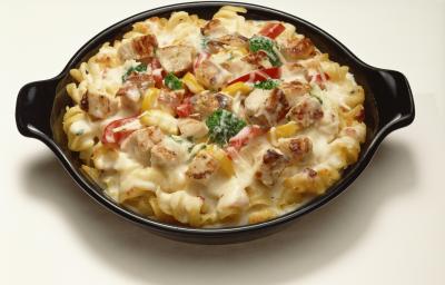 Fotografia de um macarrão cremoso, tipo parafuso, com creme de leite, tomate e manjericão. A pasta está dentro de um recipiente de vidro na cor preta, que está sobre uma mesa branca.