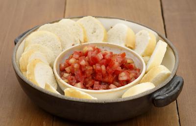 Fotografia em tons de vermelho em uma bancada de madeira com uma panela preta de ferro com alças laterais e vários pães fatiados com um potinho de molhinho de tomate. Fotografia em tons de vermelho em uma bancada de madeira com uma panela preta de ferro com alças laterais e vários pães fatiados com um potinho de molhinho de tomate.