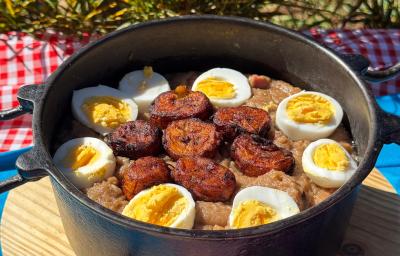 Fotografia de uma panela preta de barro com tutu de feijão com rodelas de ovo cozido por cima, ao lado de banana da terra frita. Fotografia de uma panela preta de barro com tutu de feijão com rodelas de ovo cozido por cima, ao lado de banana da terra frita.