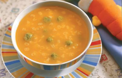 Fotografia em tons de laranja em uma mesa com uma toalha de folhas, um prato raso colorido, um prato fundo redondo colorido com a sopa divertida com bolinhas de espinafre. Fotografia em tons de laranja em uma mesa com uma toalha de folhas, um prato raso colorido, um prato fundo redondo colorido com a sopa divertida com bolinhas de espinafre.