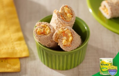 Enroladinhos de pão recheados com cenoura e ovo cremosos, cortados em pedaços e servidos em tigela verde, sobre mesa clara.