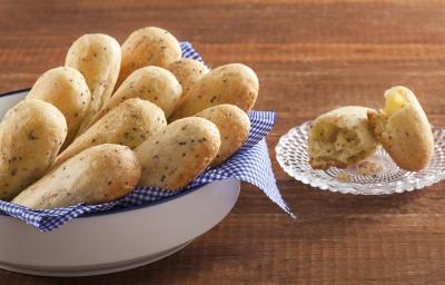 Fotografia em tons de dourado, branco e marrom, com recipiente branco contendo onze pãezinhos assados sobre guardanapo quadriculado em branco e azul, ao lado pratinho com pão aberto ao meio, tudo sobre bancada de madeira. Fotografia em tons de dourado, branco e marrom, com recipiente branco contendo onze pãezinhos assados sobre guardanapo quadriculado em branco e azul, ao lado pratinho com pão aberto ao meio, tudo sobre bancada de madeira.