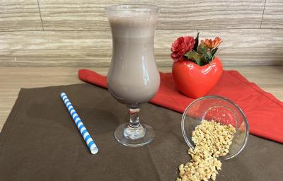 Fotografia em tons de vermelho e marrom com uma taça ao centro. Dentro da taça existe uma bebida cremosa de leite com NESCAU Extra Cacau e Iogurte. Ao lado existe um pote com amendoins Fotografia em tons de vermelho e marrom com uma taça ao centro. Dentro da taça existe uma bebida cremosa de leite com NESCAU Extra Cacau e Iogurte. Ao lado existe um pote com amendoins
