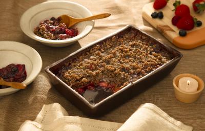 Foto em tons de marrom da receita de doce de aveia com frutas vermelhas servida em uma forma de madeira marrom escura com dois pratos fundos brancos ao lado com porções do doce Foto em tons de marrom da receita de doce de aveia com frutas vermelhas servida em uma forma de madeira marrom escura com dois pratos fundos brancos ao lado com porções do doce