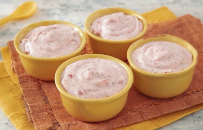 imagem mostra quatro copinhos amarelos contendo um creme de morangos em tons rosados dispostos sobre um paninho laranja