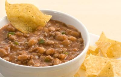 Fotografia de um bowl branco com chilli dentro, grãos de feijão da superfície e servido com tortilhas de milho ao lado no prato branco. Fotografia de um bowl branco com chilli dentro, grãos de feijão da superfície e servido com tortilhas de milho ao lado no prato branco.