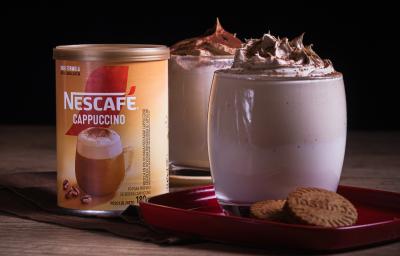 Foto da receita de cappuccino super cremoso servida em dois copos de vidro sobre uma louça vermelha em cima de uma mesa de madeira