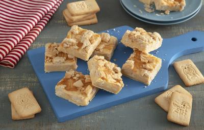 Foto em tons de bege da receita de doce de micro-ondas de biscoito passatempo servida em diversas porções sobre uma tábua azul com algumsa unidades de biscoito passatempo leite em volta. Ao fundo um paninho listrado vermelho e branco e um prato azul Foto em tons de bege da receita de doce de micro-ondas de biscoito passatempo servida em diversas porções sobre uma tábua azul com algumsa unidades de biscoito passatempo leite em volta. Ao fundo um paninho listrado vermelho e branco e um prato azul