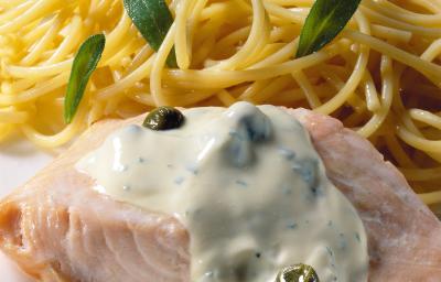 Uma mesa azul com bolinhas brancas vista de cima, um prato quadrado branco com macarrão espaguete, um pedaço de salmão com molho branco por cima. Uma mesa azul com bolinhas brancas vista de cima, um prato quadrado branco com macarrão espaguete, um pedaço de salmão com molho branco por cima.