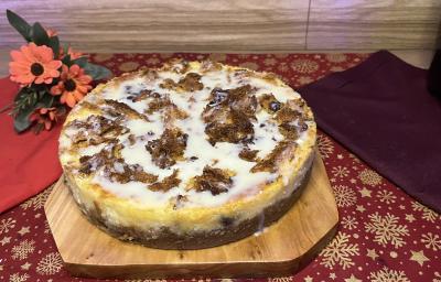 Fotografia em tons de vermelho com uma bandeja de madeira ao centro. Dentro da bandeja existe uma receita de cheesecake coberto de panettone talento e chocolate galak