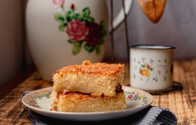 Foto da receita de Bolo de Arroz Cozido. Observa-se 3 fatias retangulares de bolo empilhadas e, atrás, um cafézinho para acompanhar. Foto da receita de Bolo de Arroz Cozido. Observa-se 3 fatias retangulares de bolo empilhadas e, atrás, um cafézinho para acompanhar.