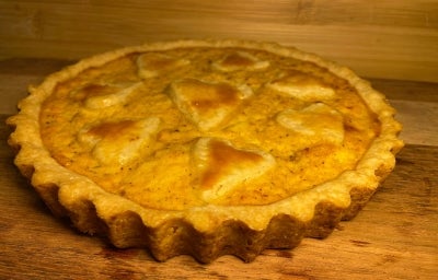 Fotografia em tons amarelados da luz de uma torta recheada de fricassé feita em forma redonda com bordinhas desenhadas, sobre uma tábua de madeira. Fotografia em tons amarelados da luz de uma torta recheada de fricassé feita em forma redonda com bordinhas desenhadas, sobre uma tábua de madeira.