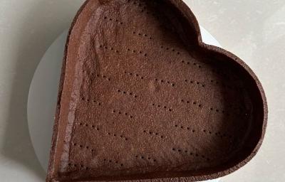 Fotografia em tons claros de uma massa de torta sabor chocolate em um prato branco raso sobre uma mesa branca.