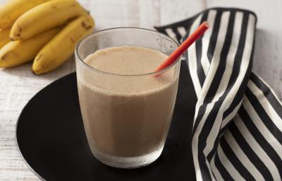 Fotografia em tons de branco e preto de uma bancada de madeira branca com um prato preto, sobre ele um copo de vidro com a bebida cremosa e um canudo vermelho. Ao lado um paninho listrado branco e preto e um cacho de banana. Fotografia em tons de branco e preto de uma bancada de madeira branca com um prato preto, sobre ele um copo de vidro com a bebida cremosa e um canudo vermelho. Ao lado um paninho listrado branco e preto e um cacho de banana.