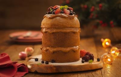Foto de um panettone cortado em três camadas, com um recheio em tom de marrom claro. Ele está sobre uma tábua de madeira há decorações de natal Foto de um panettone cortado em três camadas, com um recheio em tom de marrom claro. Ele está sobre uma tábua de madeira há decorações de natal